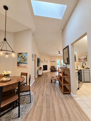 Un vaste espace de vie doté d’un haut plafond, d’une table à manger avec des chaises, d’une cheminée et d’une vue sur la cuisine grâce à une arche ouverte.
