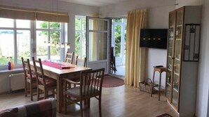 Ein Essbereich mit Tisch und Stühlen, einem an der Wand montierten Fernseher und Blick ins Freie durch große Fenster.