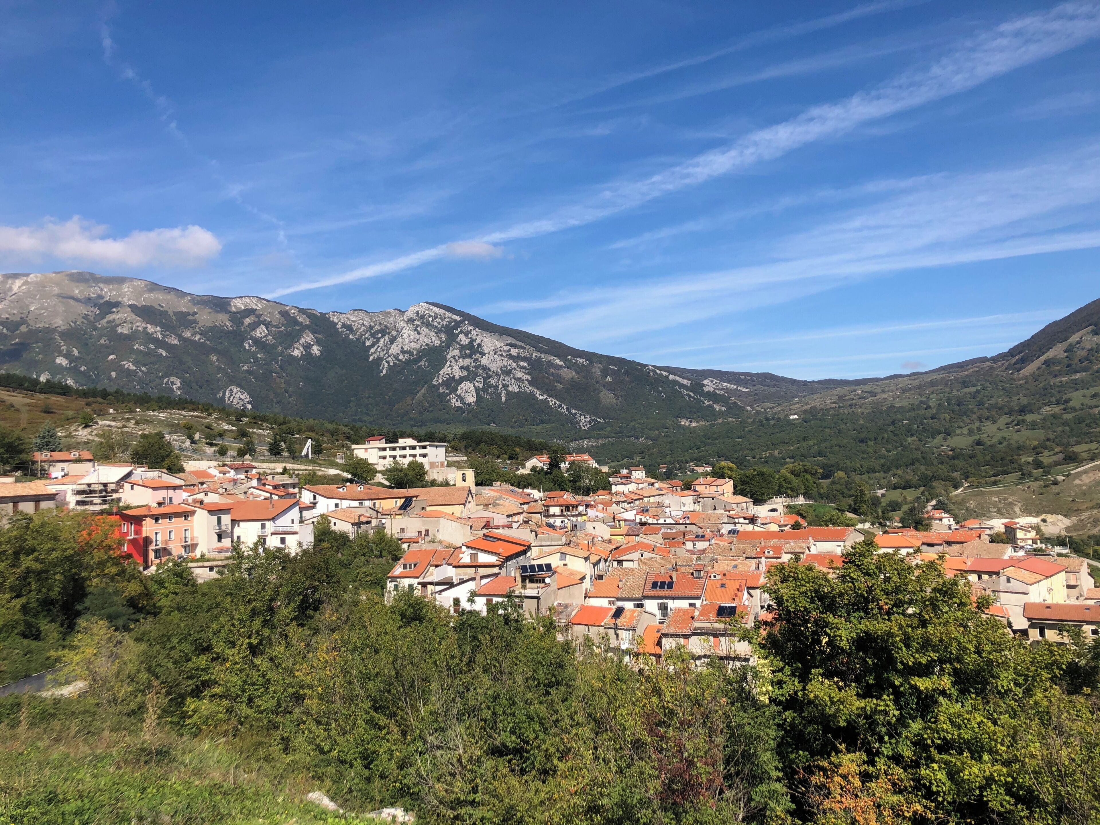A town with red-roofed buildings, surrounded by mountains and greenery.