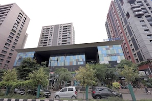 A modern building with a glass facade, surrounded by tall residential buildings. - Palm Greens Suites & Banquet (Surat)