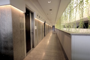 A hallway with a series of doors, a tiled floor, and a wall with hanging plants. - Palm Greens Suites & Banquet (Surat)