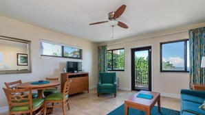 Ein Wohnzimmer mit Esstisch, Stühlen, einem Fernseher, Deckenventilator und Blick ins Freie.