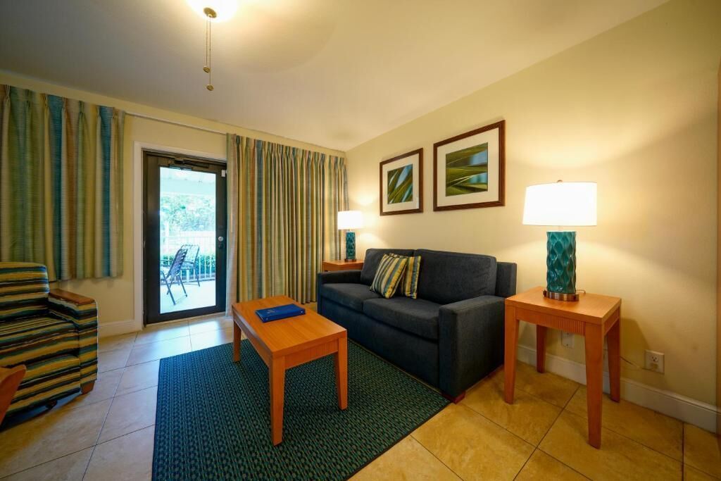Sala de estar con un sofá, una mesa de centro, un sillón a rayas, dos lámparas y vistas a través de un ventanal.