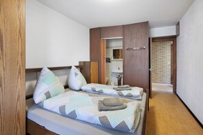 Ein Schlafzimmer mit zwei Betten, einem Holzschrank und einem durch eine offene Tür einsehbaren Badezimmer.