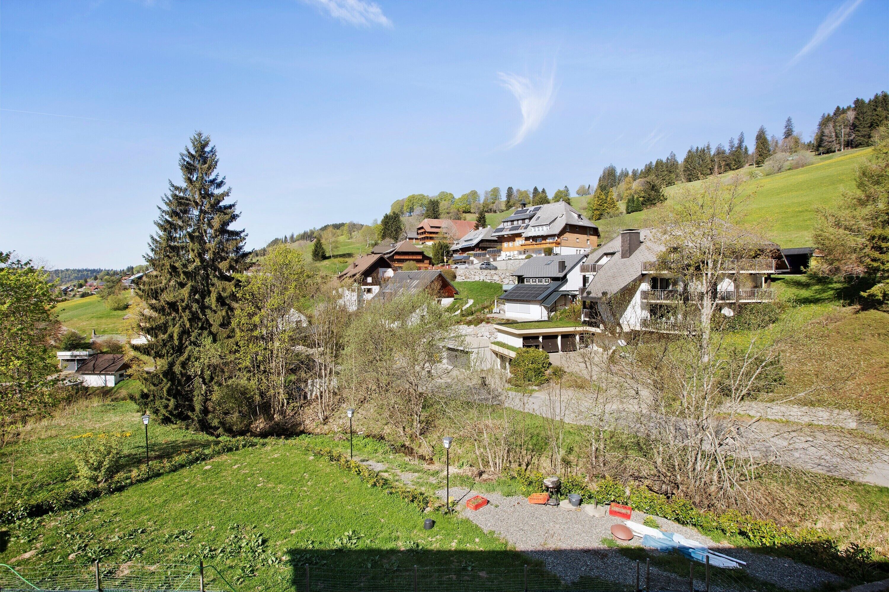 A hillside village with traditional wooden houses, a large coniferous tree, and a clear sky.
