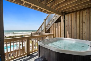 Eine Holzterrasse mit Whirlpool, einer Holztreppe und Blick auf den Strand.