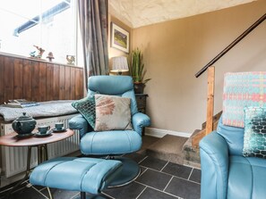 Una habitación acogedora con un sillón azul, una mesita con un hervidor de agua y una escalera.