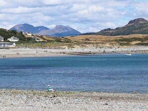 Eine Küstenlandschaft mit einem felsigen Strand, einer Person am Ufer und Häusern im Hintergrund.