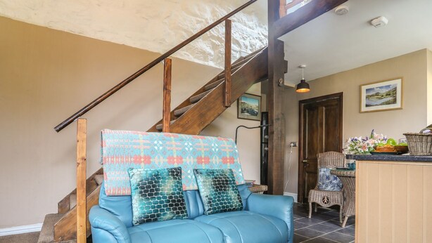 A blue leather sofa with patterned cushions, a wooden staircase, a wicker chair, and a framed landscape painting. - Ty Gwenno (Criccieth)