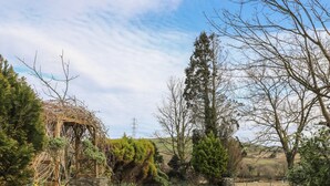 A rural pathway leading to a stone wall with a wooden gate, surrounded by greenery and a clear sky. - Ty Gwenno (Criccieth)
