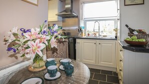 A kitchen with white cabinets, a stainless steel range hood, a window with a view, and a table with a floral arrangement and tea set. - Ty Gwenno (Criccieth)