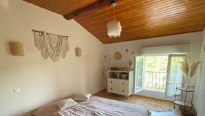 A bedroom with a wooden ceiling, a bed with a patterned bedspread, a dresser, and a window with a view. - Apartment near the sea and Montpellier (Pignan)