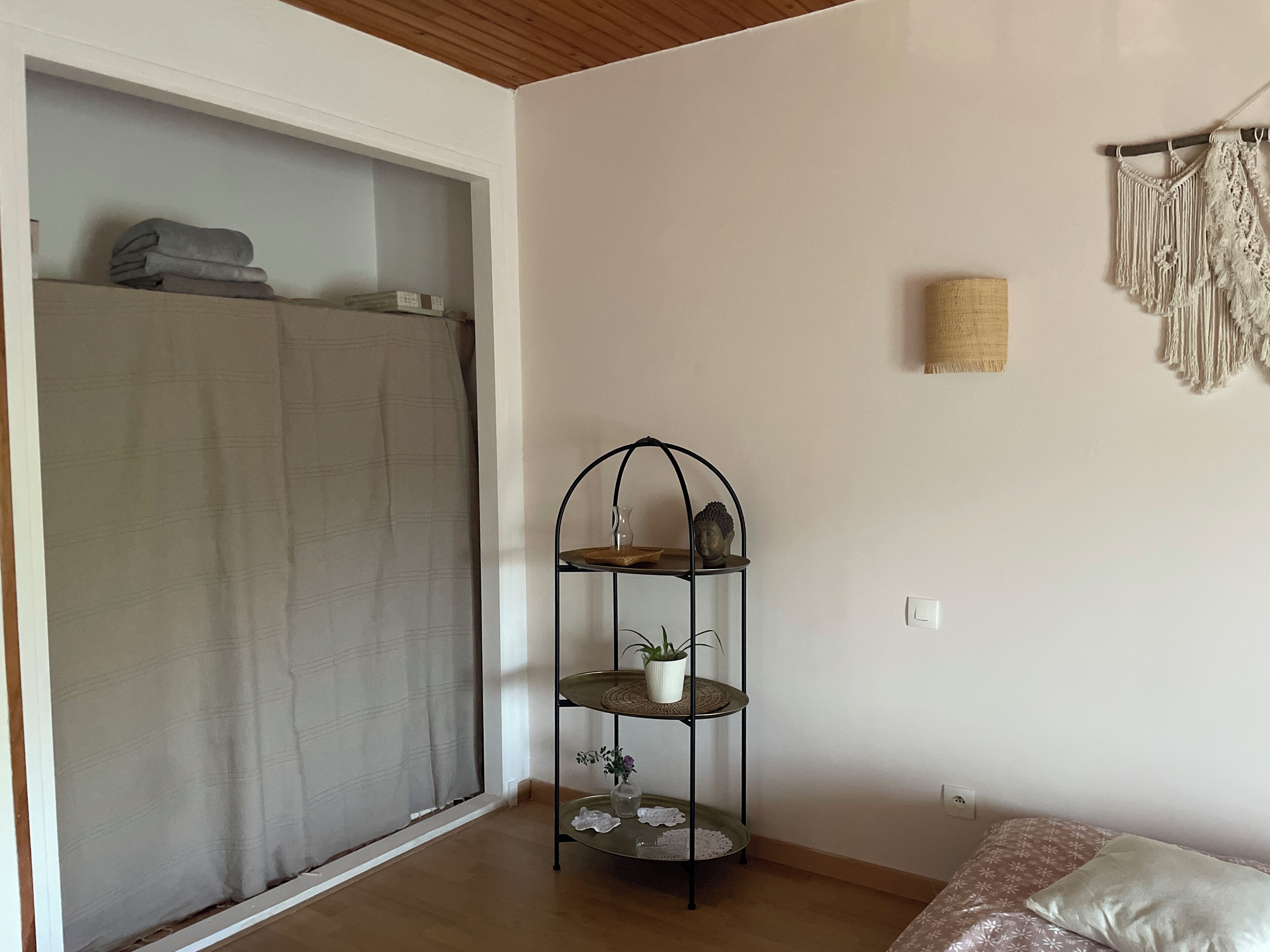 Ein Zimmer mit einem Bett, einem Regal mit Dekoration, einem Vorhang und einem Wandbehang aus Makramee.
