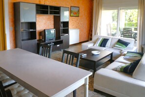 Ein Wohnzimmer mit Sofa, Fernseher, Esstisch und Küchenzeile mit Schränken.
