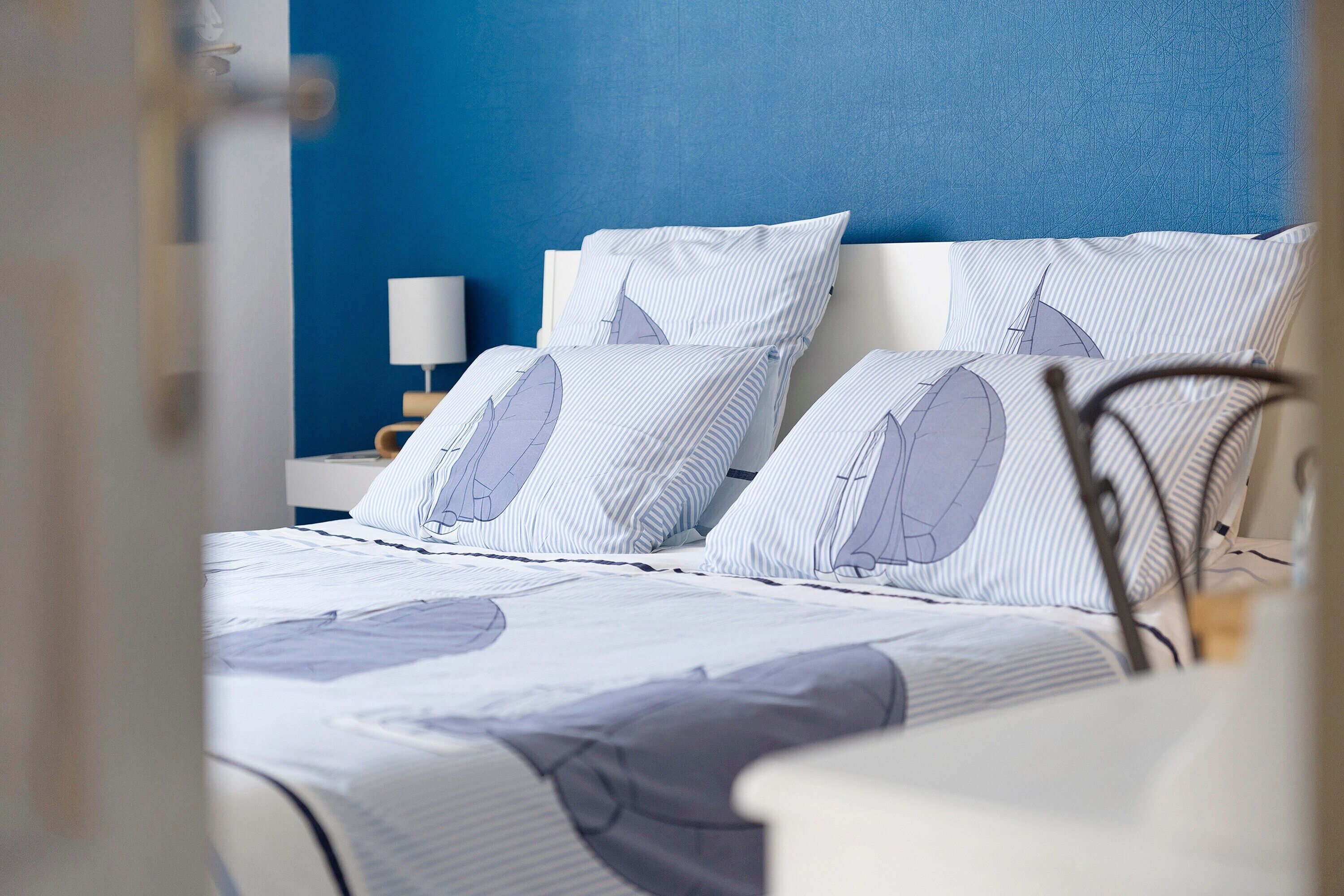 A bed with striped bedding and a headboard, a bedside table with a lamp, and a blue wall.