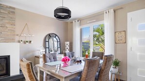 A dining area with wicker chairs, a table with a vase of flowers, and a view through a glass door. - Guest Room “Chambre Saint-Samson-sur-Rance” with Private Terrace, Garden & Wi-Fi (Saint-Samson-sur-Rance)
