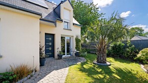 A house with a paved driveway, a small patio with outdoor furniture, and a well-maintained garden with a palm tree. - Guest Room “Chambre Saint-Samson-sur-Rance” with Private Terrace, Garden & Wi-Fi (Saint-Samson-sur-Rance)