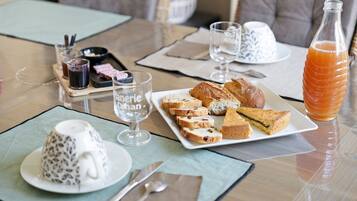 Une table mise pour le petit-déjeuner, avec une assiette de viennoiseries, une bouteille de jus d’orange et une tasse de café.