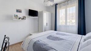 A bedroom with a bed, a TV, a wardrobe, and a window with curtains. - Guest Room “Chambre Saint-Samson-sur-Rance” with Private Terrace, Garden & Wi-Fi (Saint-Samson-sur-Rance)