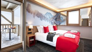 A hotel room with a bed, a small table with a lamp, a nightstand, a large window, and a wall mural. - Mountain-ready Apartment for 6 (La Plagne-Tarentaise)