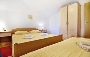 Ein Einzelbett mit Holz-Kopfteil, ein Nachttisch mit Lampe, ein Kleiderschrank und ein roter Teppich.