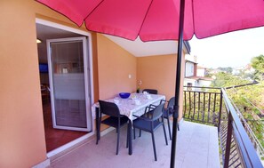 Ein Balkon mit Tisch und Stühlen, einem roten Sonnenschirm und Blick auf die Nachbarschaft.