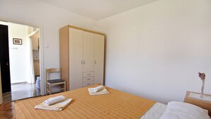 Une chambre à coucher comprenant un lit, une armoire, une chaise et une petite table sur laquelle est posé un vase.