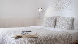 Una cama bien hecha con un edredón estampado, un par de gafas y un libro abierto encima.
