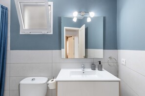 A bathroom with a white sink, a mirror with lights, a toilet, and a blue curtain. - Vacation Home with Sea Views (Breña Baja)