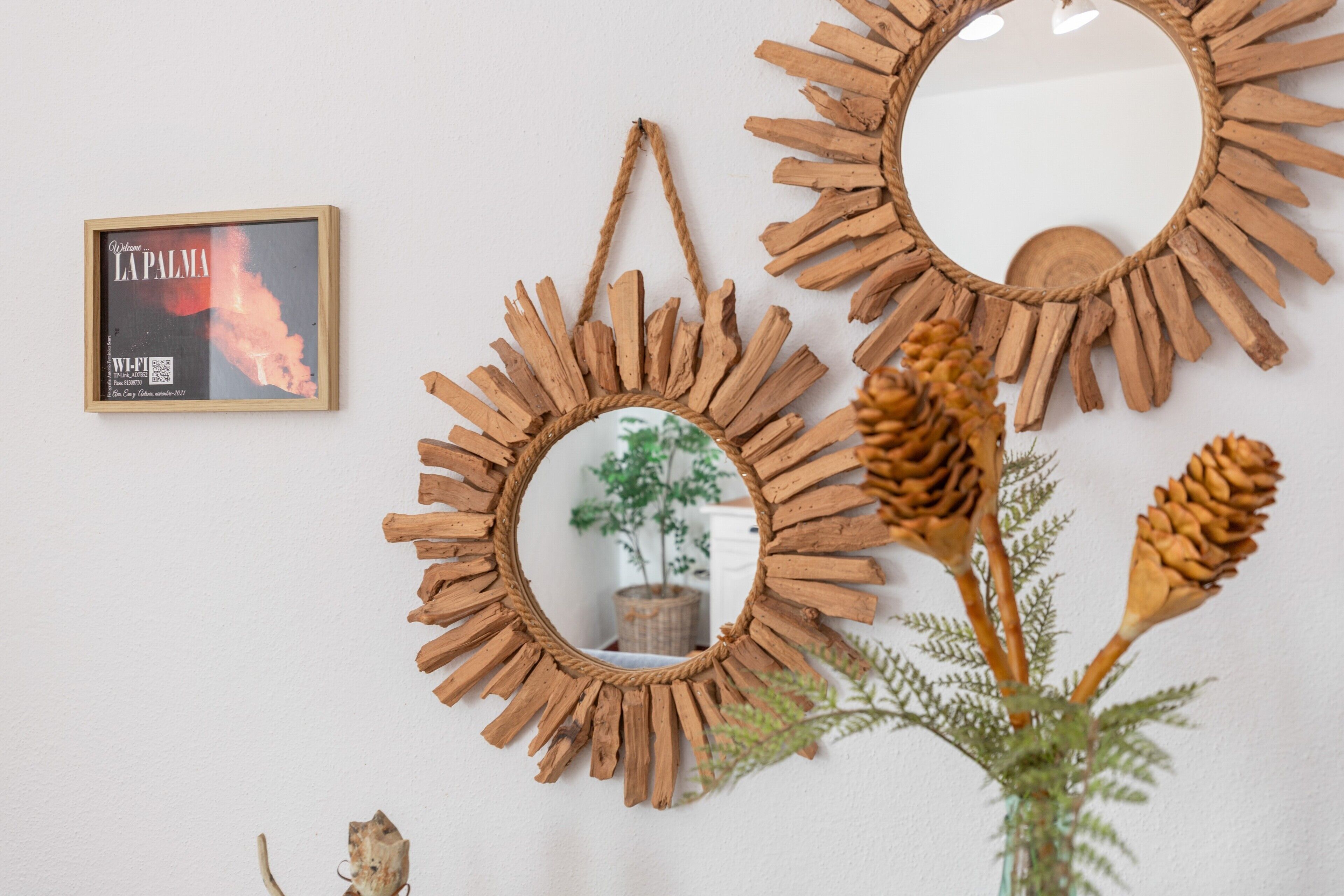 Three rustic wooden mirrors with a sunburst design, a framed picture, and a potted plant with pine cones.