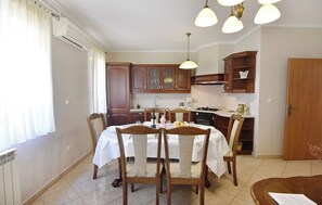 A dining area with a table set for four, wooden chairs, a kitchen with wooden cabinets, and pendant lighting. - Spacious ground-floor flat in Umag (Umag)