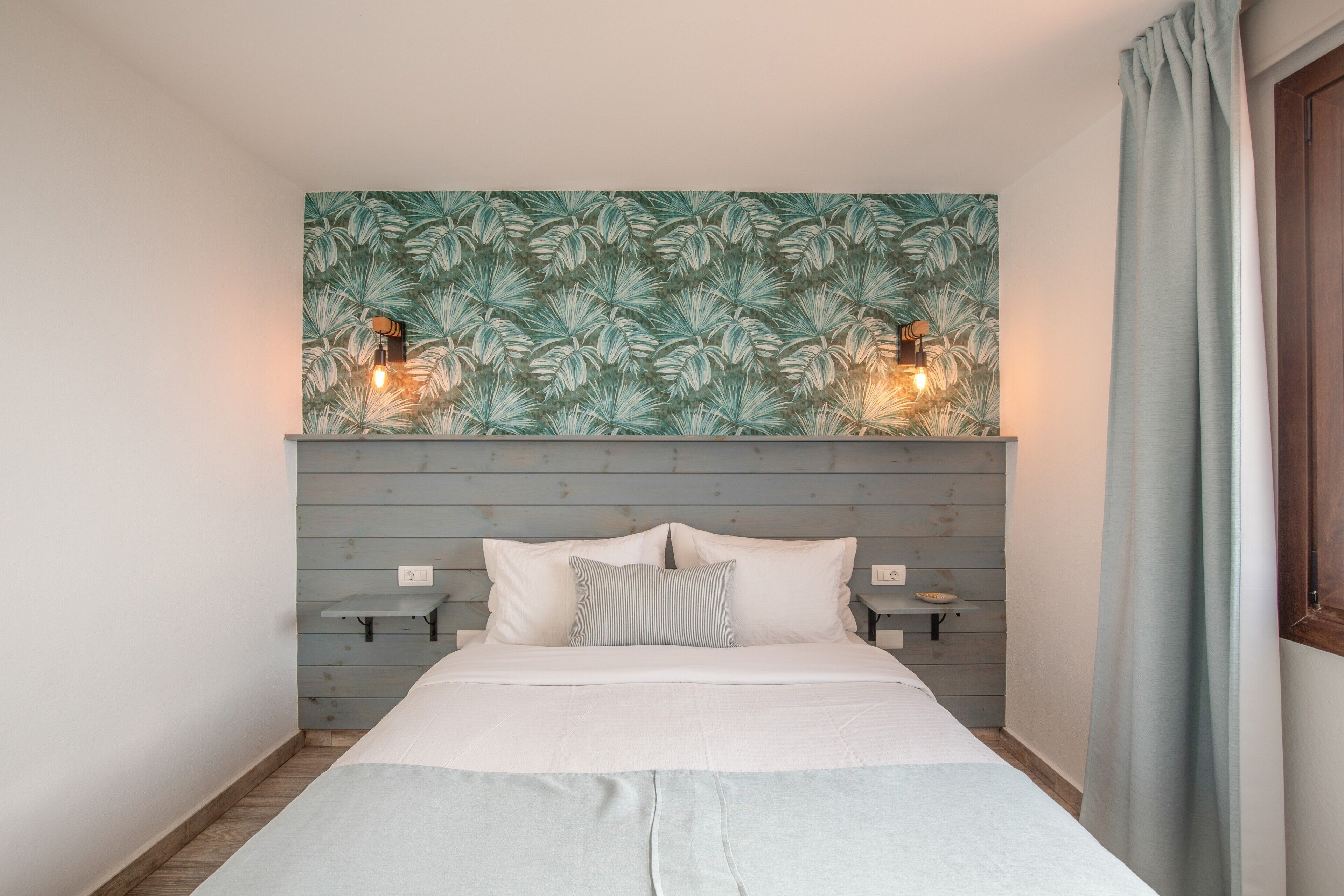 A bed with white bedding, a wooden headboard, two bedside tables, and a wall with a leaf pattern.