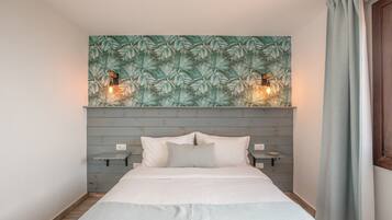 A bed with white bedding, a wooden headboard, two bedside tables, and a wall with a leaf pattern.