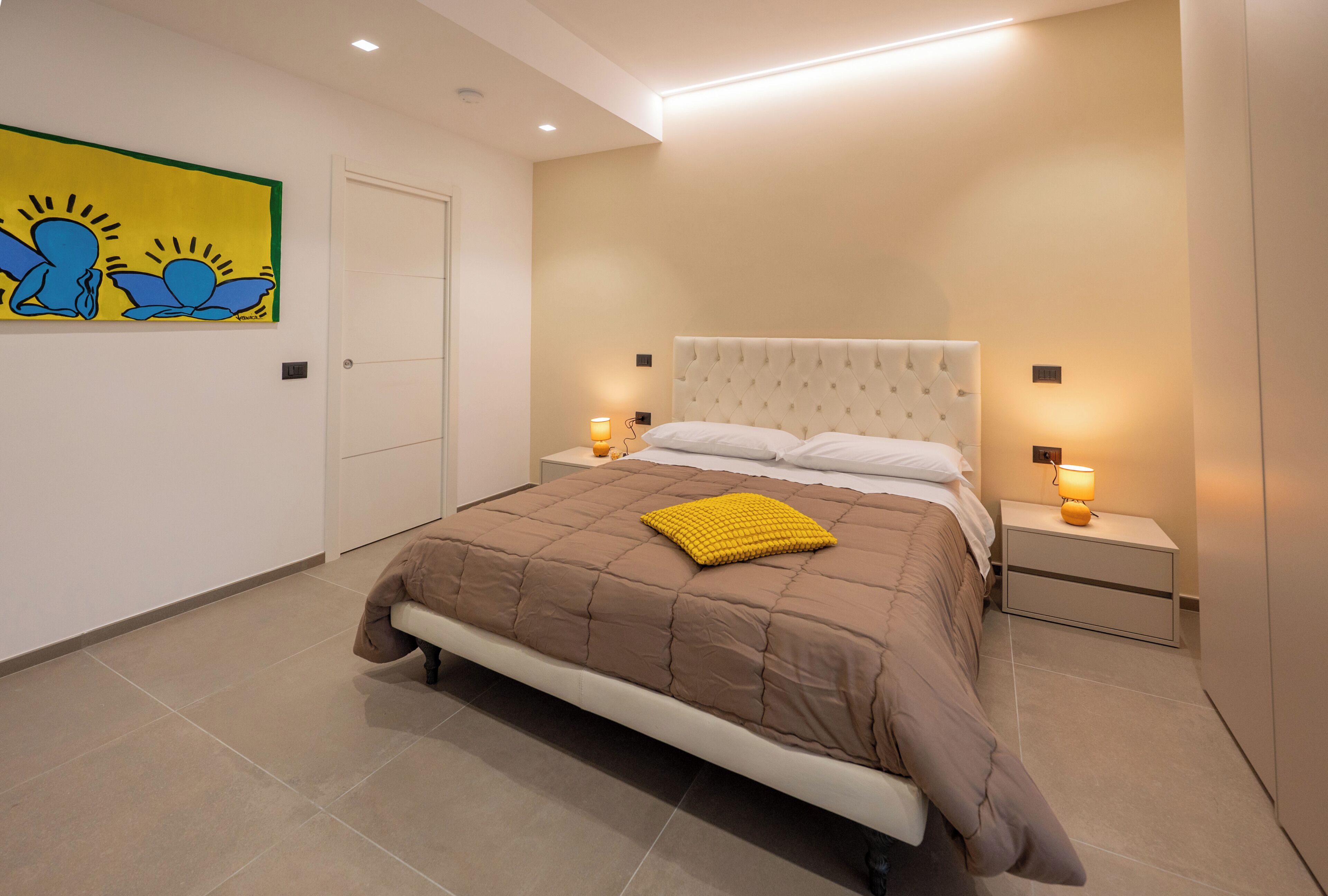 Une chambre à coucher avec un lit, des tables de chevet, une horloge murale, une porte et un tableau.