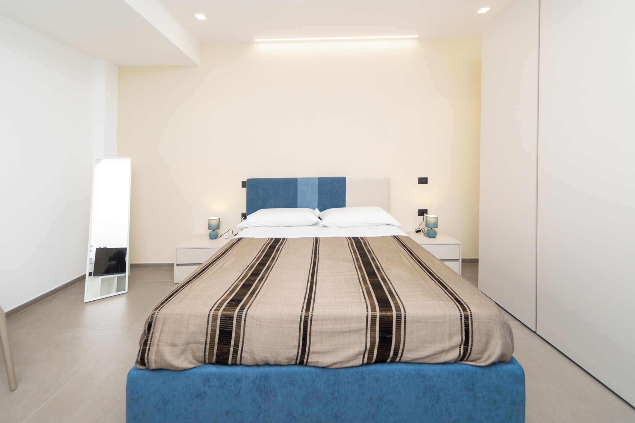 A modern bedroom with a large bed, bedside tables, and a mirror on the wall.