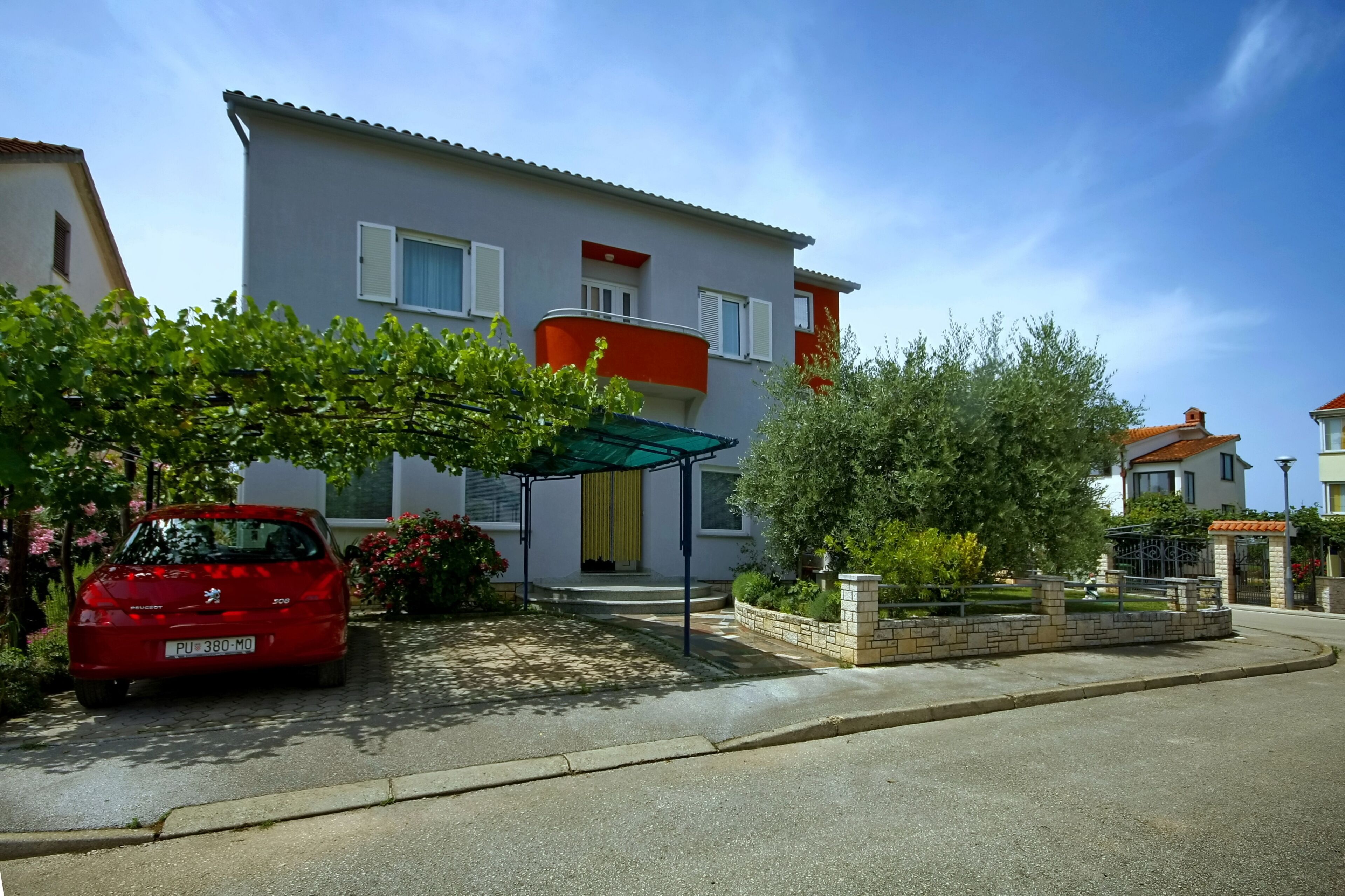 A two-story residential building with a covered entrance and a red car parked in front.