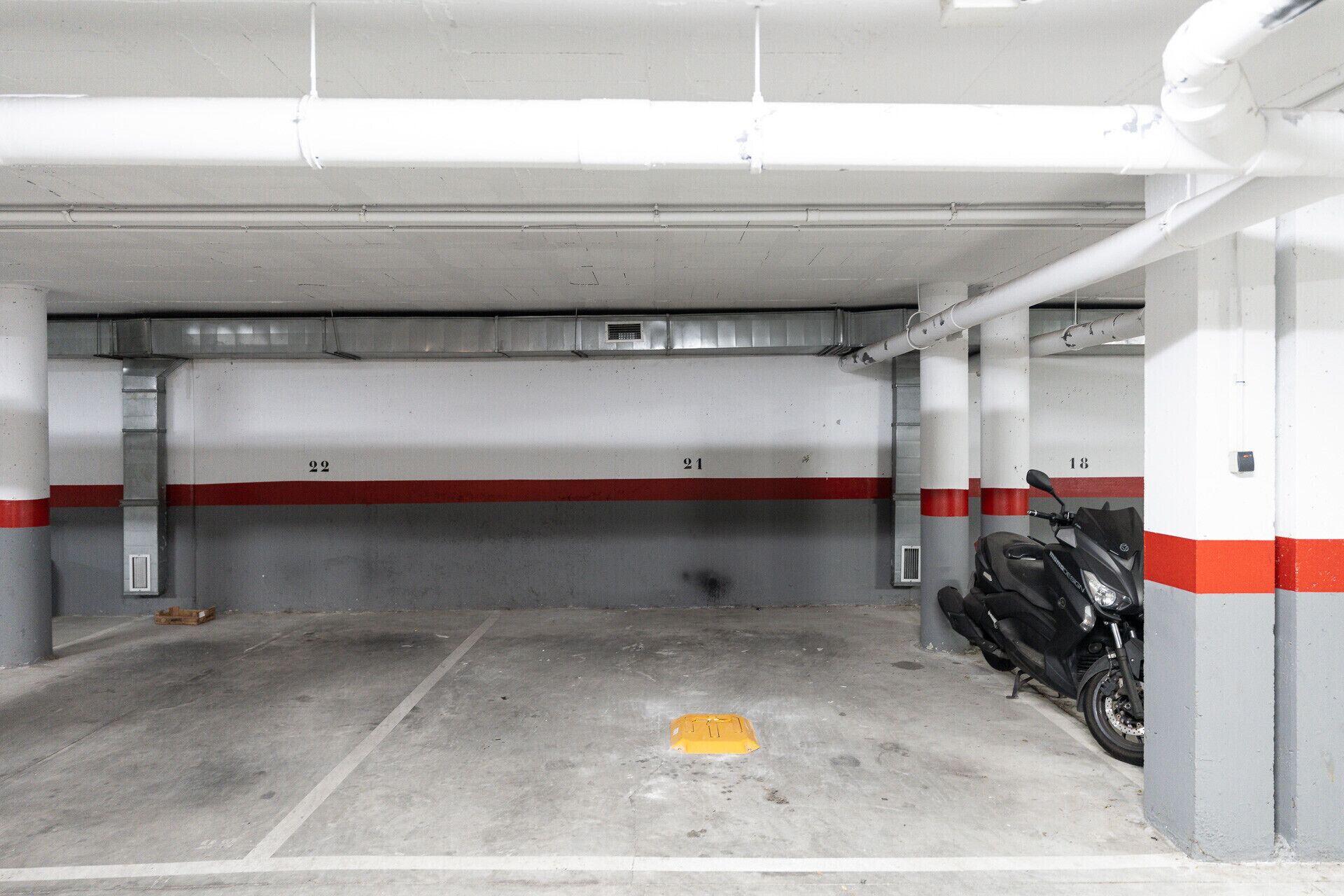 Un estacionamiento con pisos de concreto, espacios numerados y una motocicleta estacionada en uno de ellos.