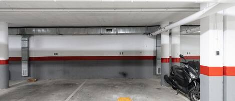 Un estacionamiento con pisos de concreto, espacios numerados y una motocicleta estacionada en uno de ellos.