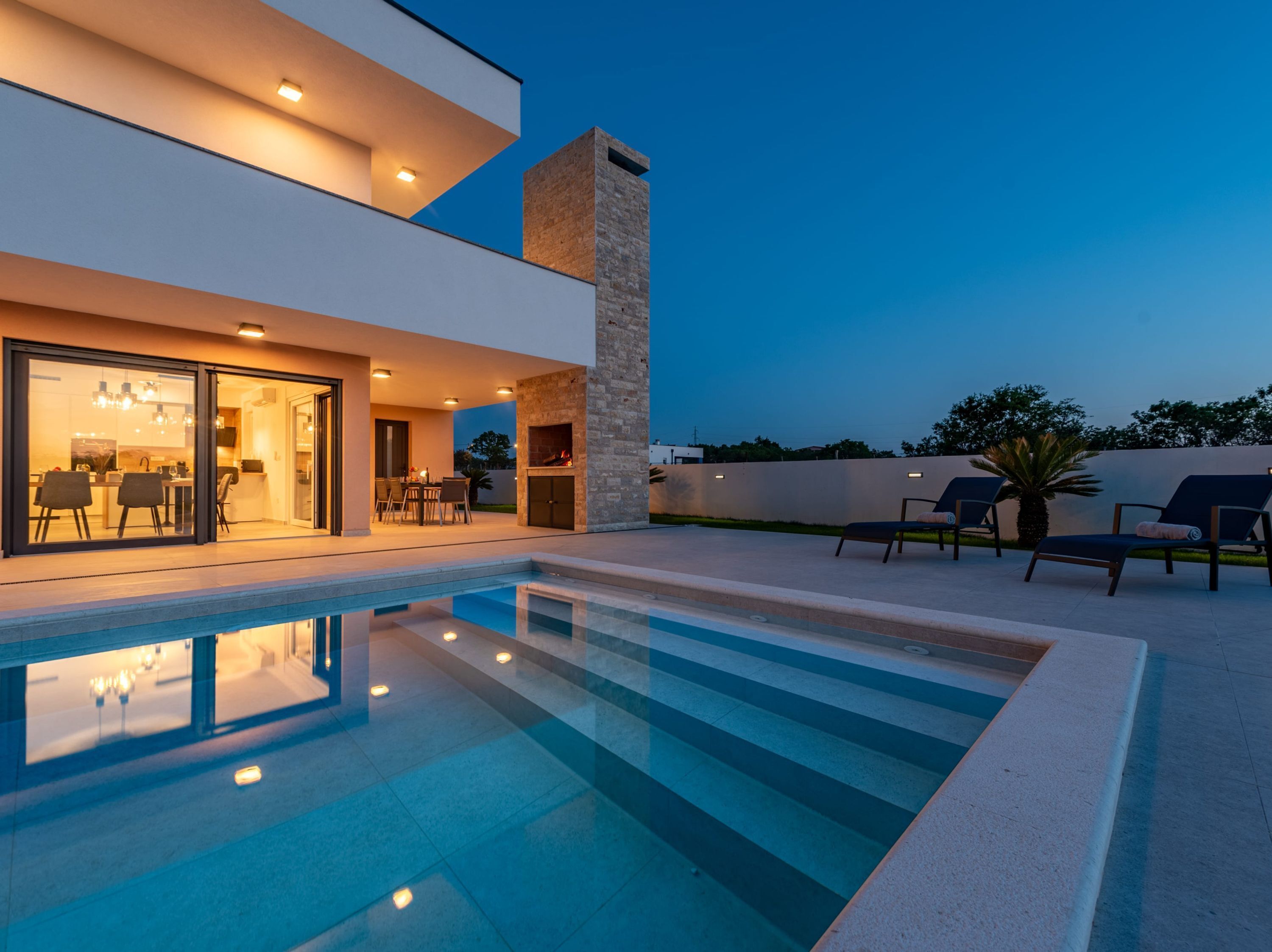 A modern house with a swimming pool, outdoor seating, and a stone fireplace.
