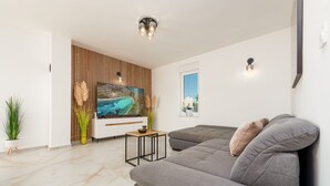 En moderne stue med et stort fladskærms-tv, en grå sofa, en trævæg og en loftlampe.