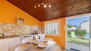 Un comedor con una mesa dispuesta para cuatro, una cocina con electrodomésticos modernos y vistas al jardín a través de un ventanal.