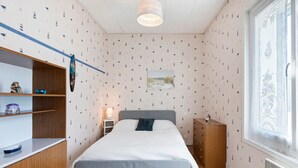 Un dormitorio con cama, armario de madera, mesita de noche, lámpara y ventana con cortina.