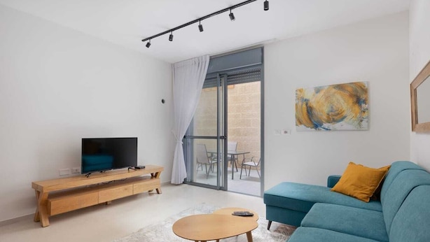 A modern living room with a TV, sofa, coffee table, and a sliding glass door leading to an outdoor area.