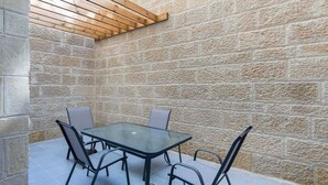 A stone-walled outdoor patio with a glass table and metal chairs.