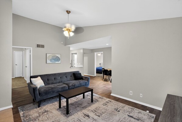 A spacious living room with a grey sofa, a coffee table, and a patterned rug.