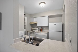 A compact kitchen with white cabinets, a stainless steel sink, a stove, and a refrigerator.