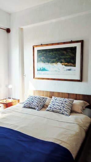 Quarto de hotel com cama, almofadas, mesa de cabeceira, abajur e um quadro na parede.