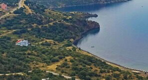 Vista aérea de uma área costeira com um edifício branco imponente, vegetação densa e um mar azul límpido.