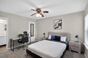 A bedroom with a bed, desk, chair, nightstands, and a ceiling fan.