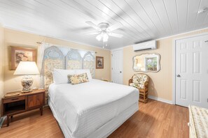 A bedroom with a bed, nightstand, lamp, chair, and a ceiling fan.